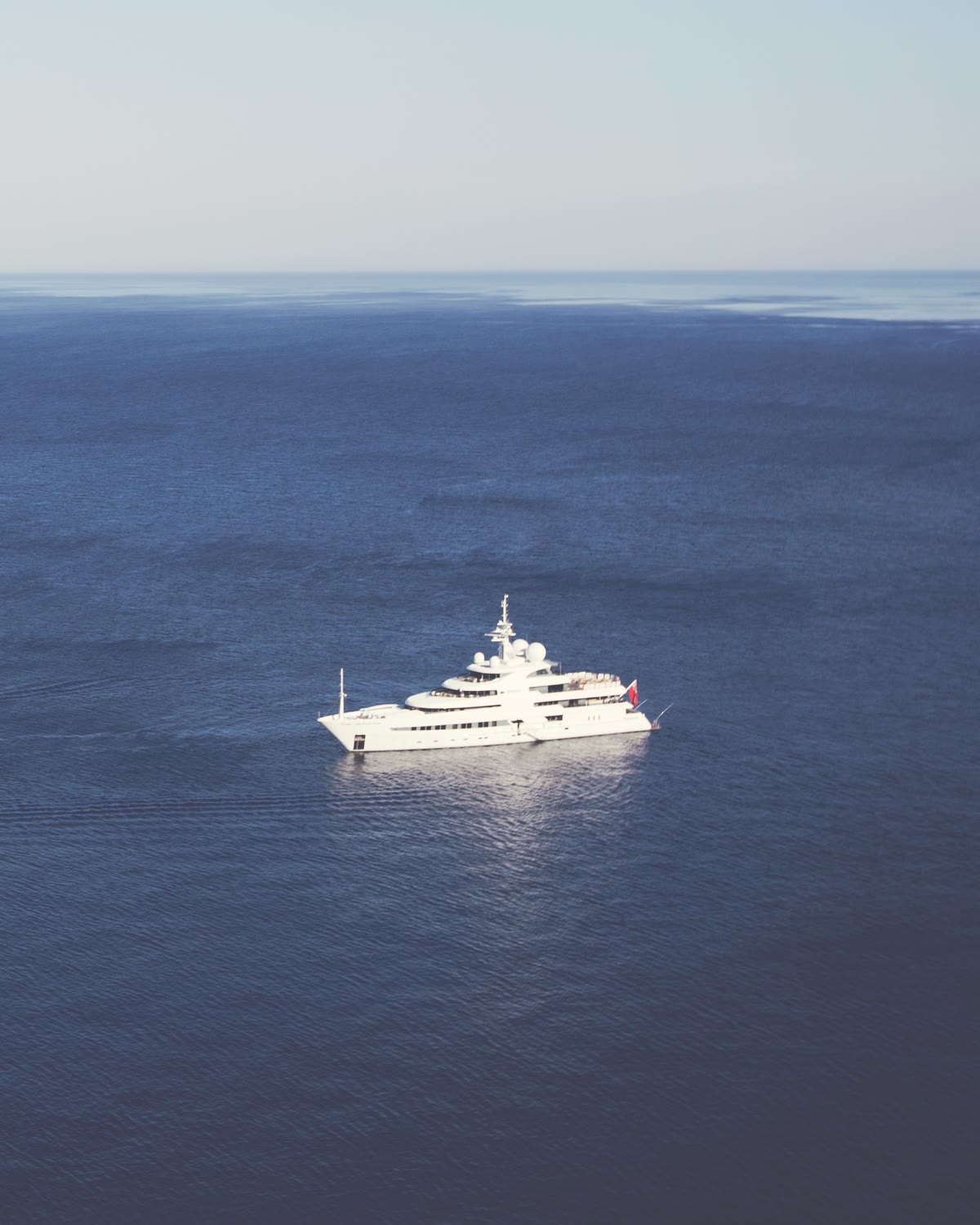 A white superyacht anchored alone on a calm, deep-blue sea