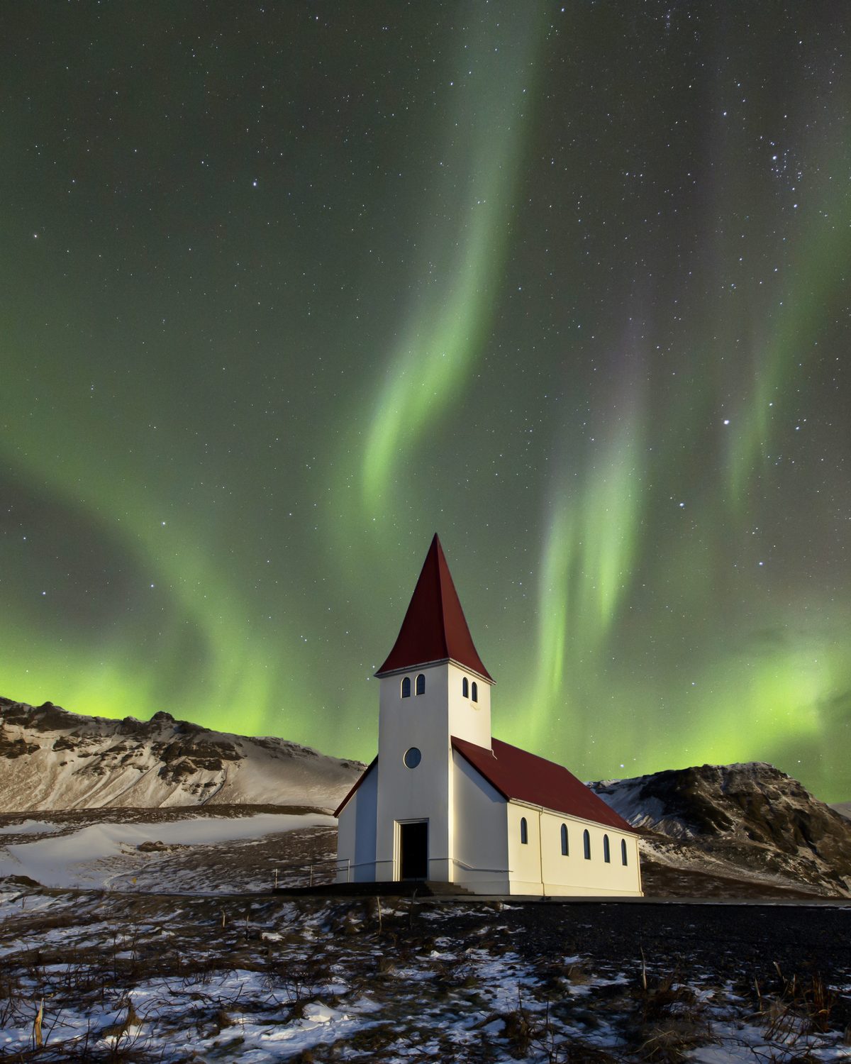 The Northern Lights rippling green above a little red-roofed church in Iceland