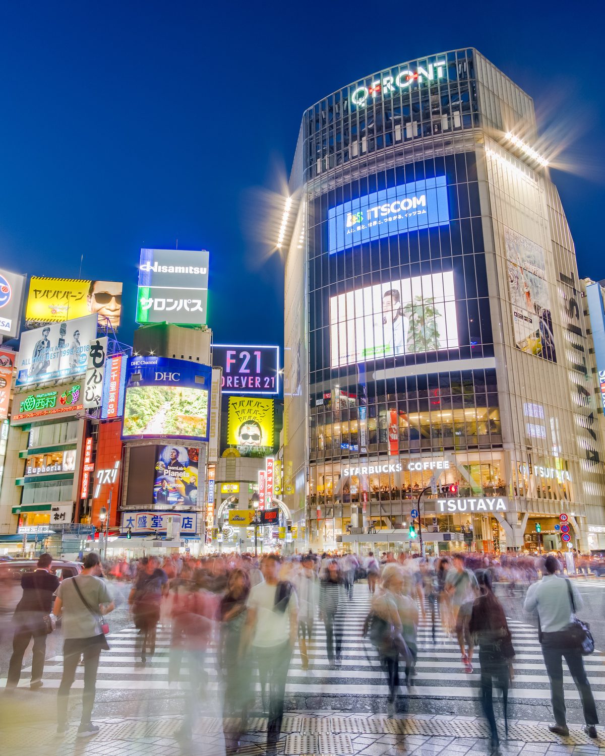 Shibuya Crossing in Tokyo at night, crowds streaming under the neon screens